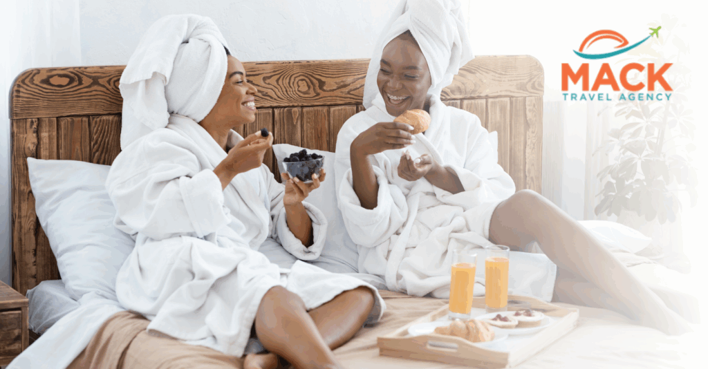 Two Black women relaxing in luxury spa robes, enjoying breakfast in bed during a rejuvenating self-care, luxury group travel trip.